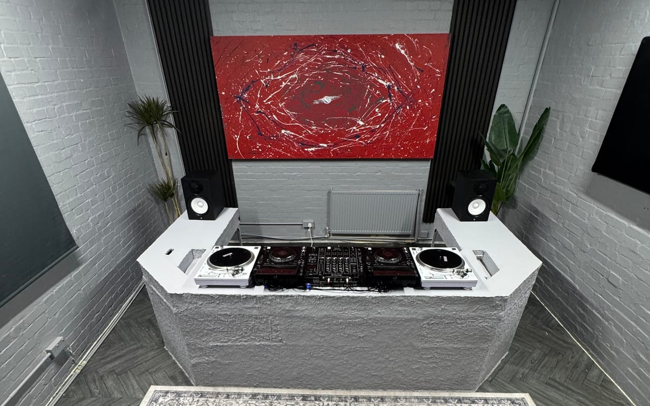 The DJ room head-on: the hand-built concrete booth carrying the full deck lineup, beneath the red canvas hung between two black acoustic slat panels