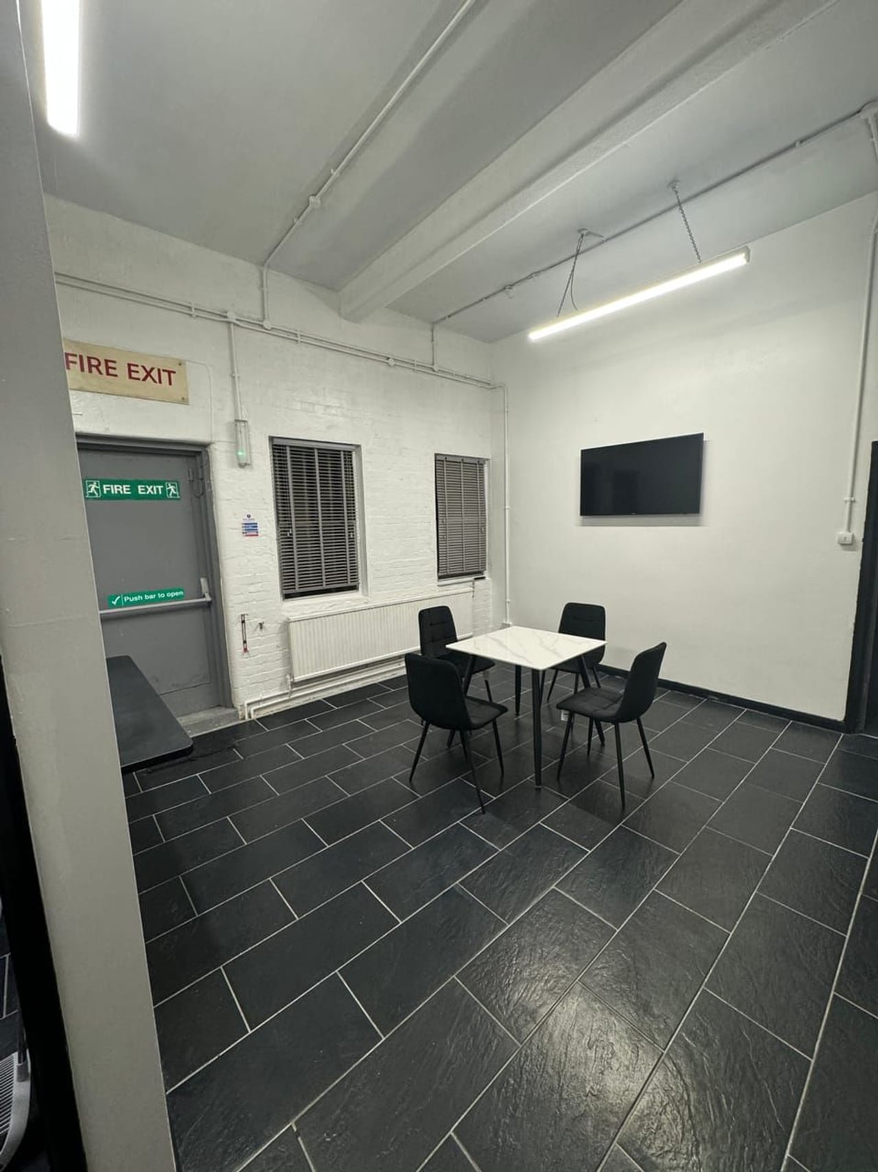 The kitchen and breakout space at Scope Media Studios: a table and chairs, a wall-mounted screen and dark tiled floor.