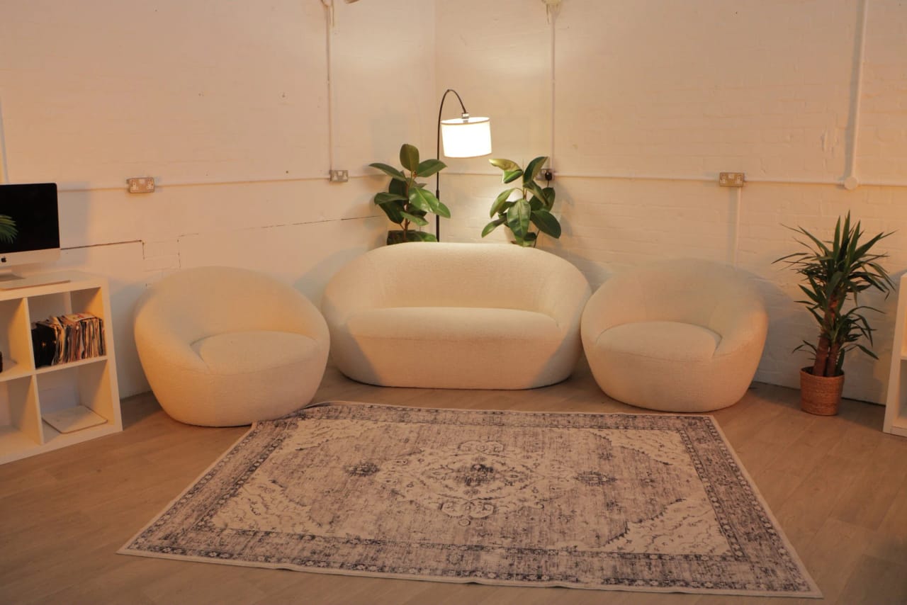 The client lounge: a cream bouclé sofa and armchairs on a patterned rug under an arc floor lamp, with plants and a television