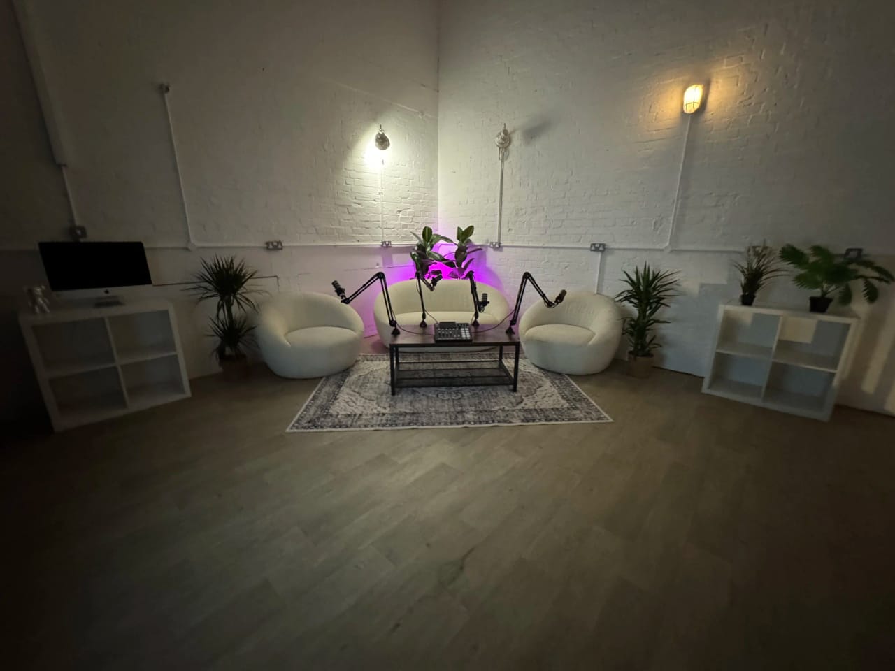 The podcast setup in the client lounge with four microphone booms around the bouclé seating under a purple accent light