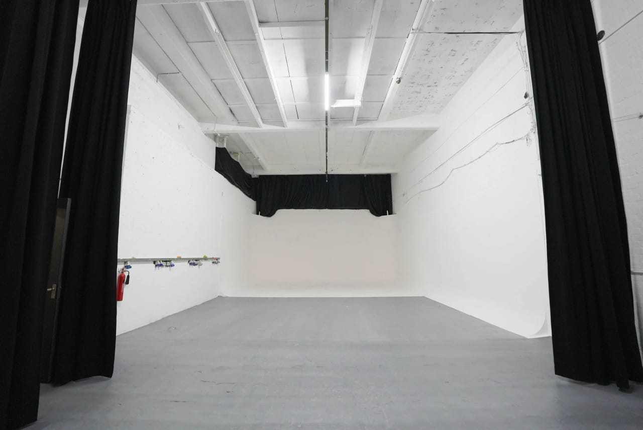 Studio A seen head-on: a white infinity cove framed between black blackout curtains, grey studio floor