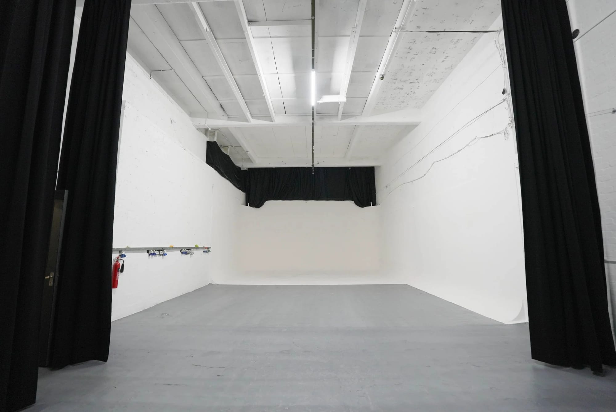 Studio A seen head-on: a white infinity cove framed between black blackout curtains, grey studio floor