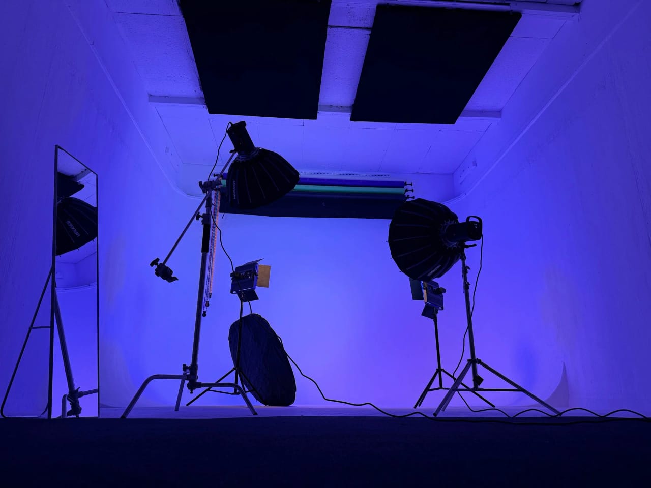 Studio B's cove lit deep blue with two para softboxes and a standing mirror at the edge of frame