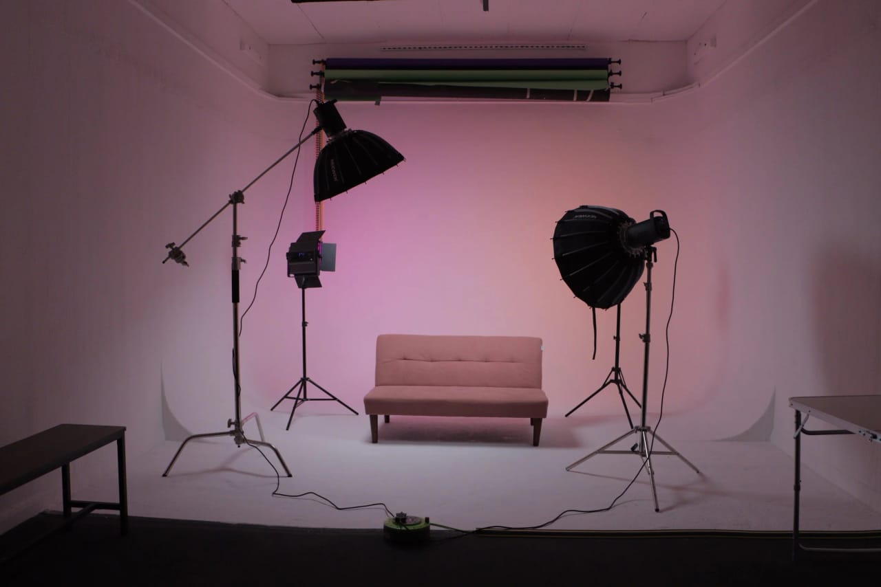 Studio B dressed for a shoot: a pink two-seater sofa on the cyclorama under a peach light wash