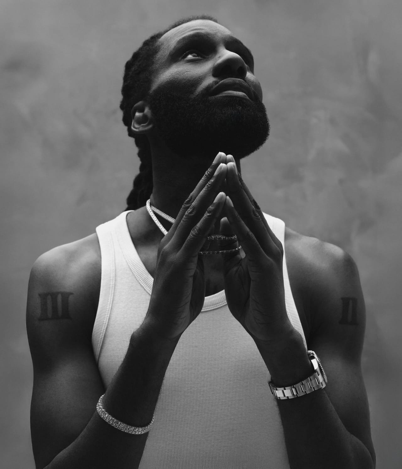 Black and white portrait, hands clasped, looking upward, on a mottled grey backdrop